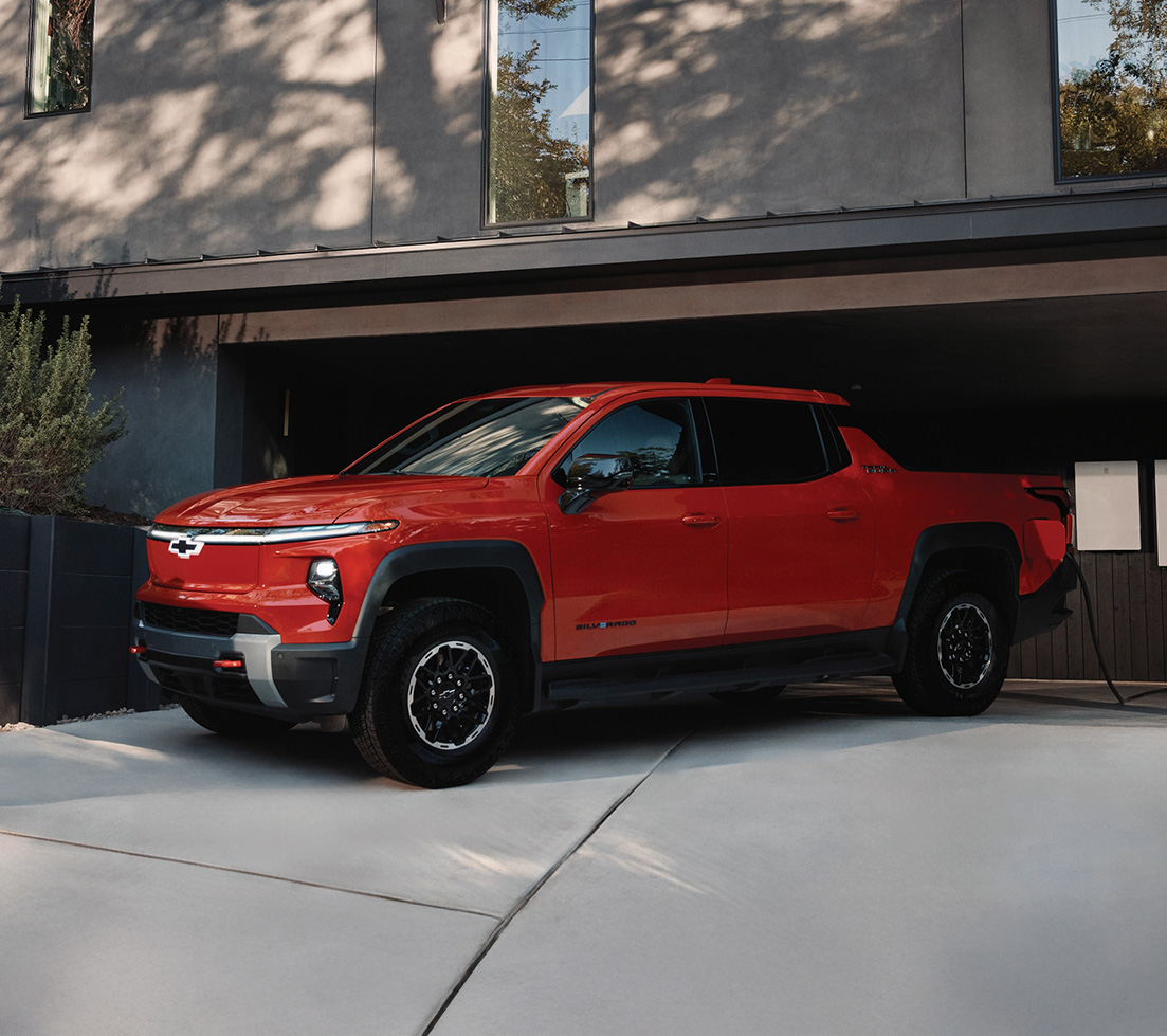 A red Chevrolet Silverado EV charging at home