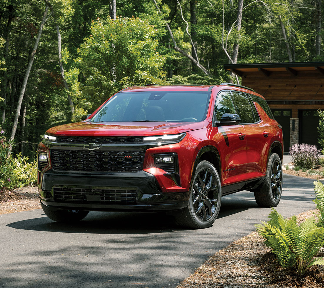A red Chevrolet Traverse parked in the driveway of a cabin in the woods