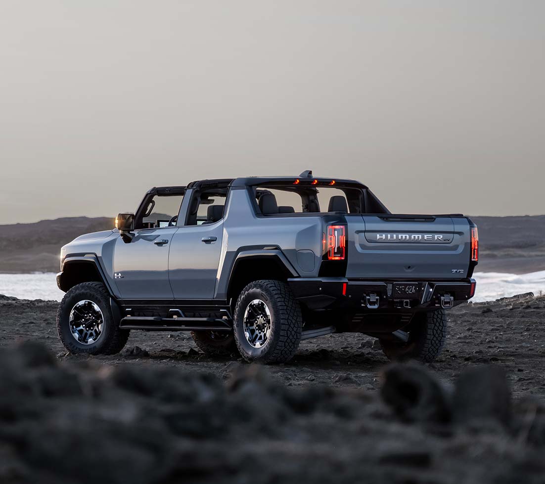 Grey GMC HUMMER EV Pickup is parked on a rocky beach near a lake