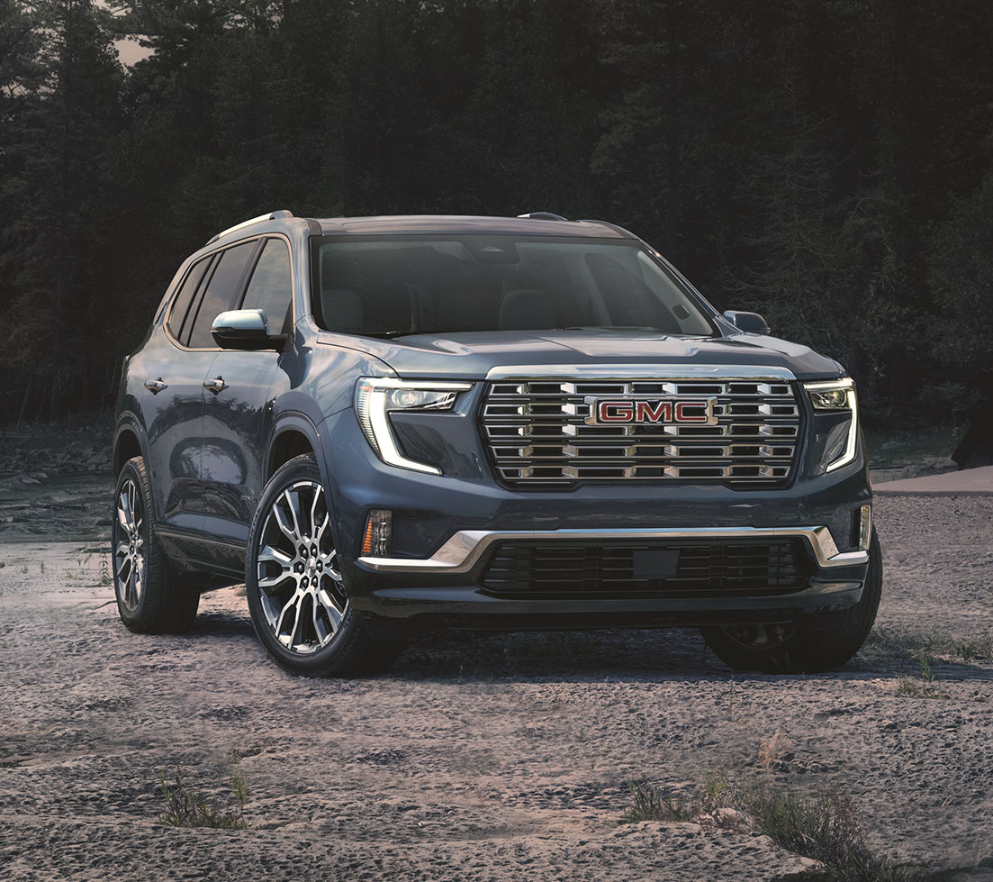A dark gray GMC Acadia parked in a rugged, forested landscape 